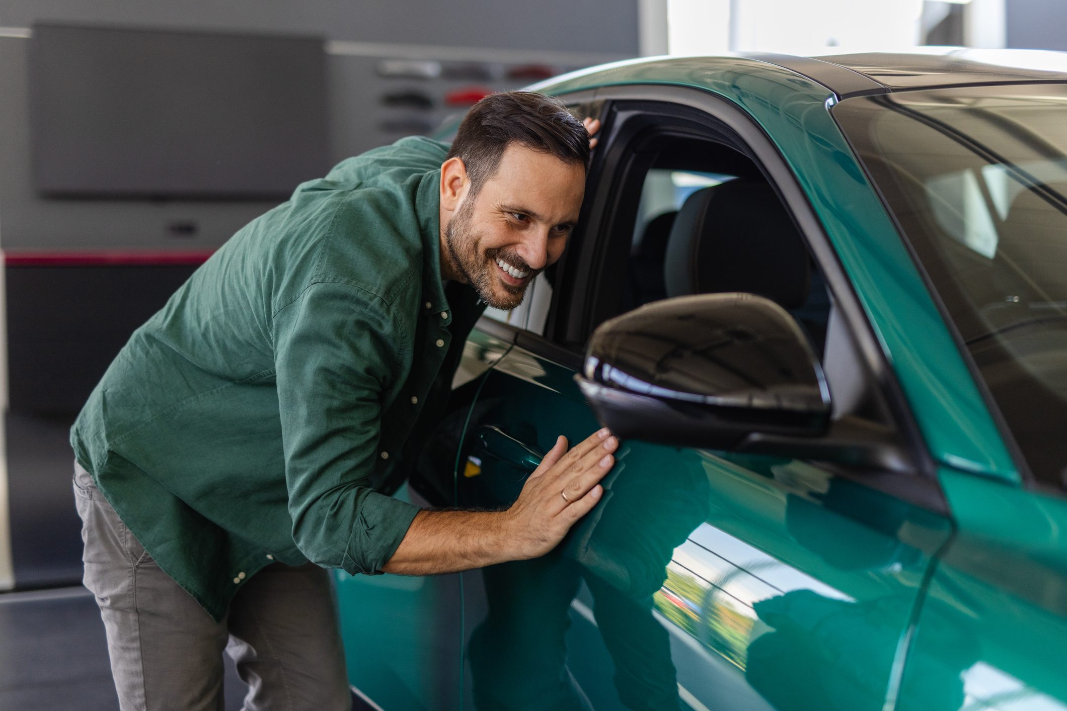 Man happily washing a green car with a sponge outdoors.